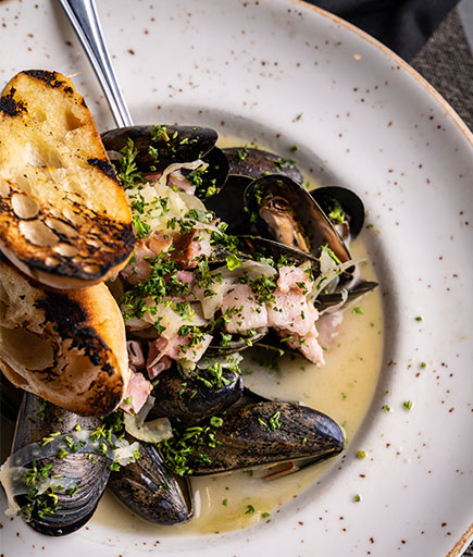 A plate of cooked mussels in broth with bread is served at Firestone's Culinary Tavern.