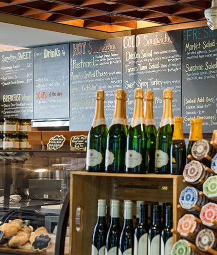 View of deli counter, menu on the chalkboard, and bottles of spirits available at Firestone's Market-to-Market.